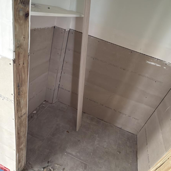 Inside a closet or niche under construction with drywall panels and a tiled floor.