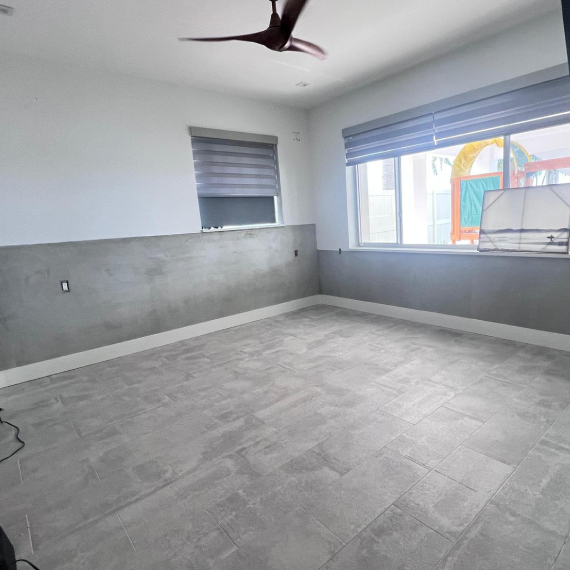 Room with gray tile, TV mounted on the gray wall, and exterior view of a play area.